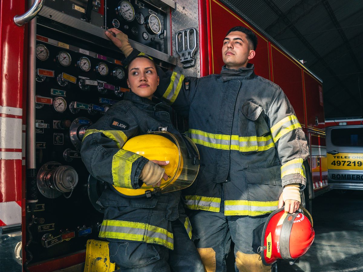 Two firefighters in full gear standing beside a fire engine