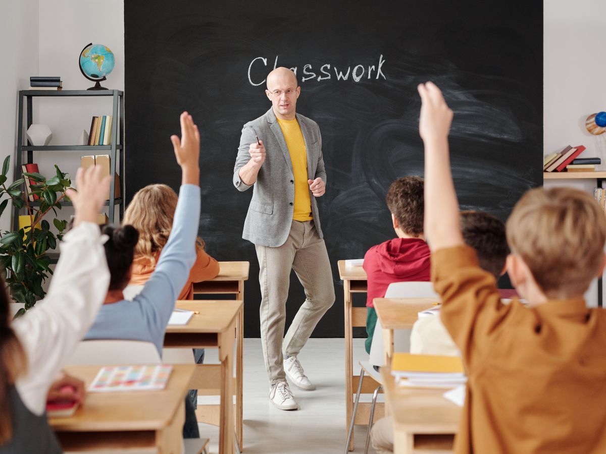 A teacher interacting with students raising their hands in class