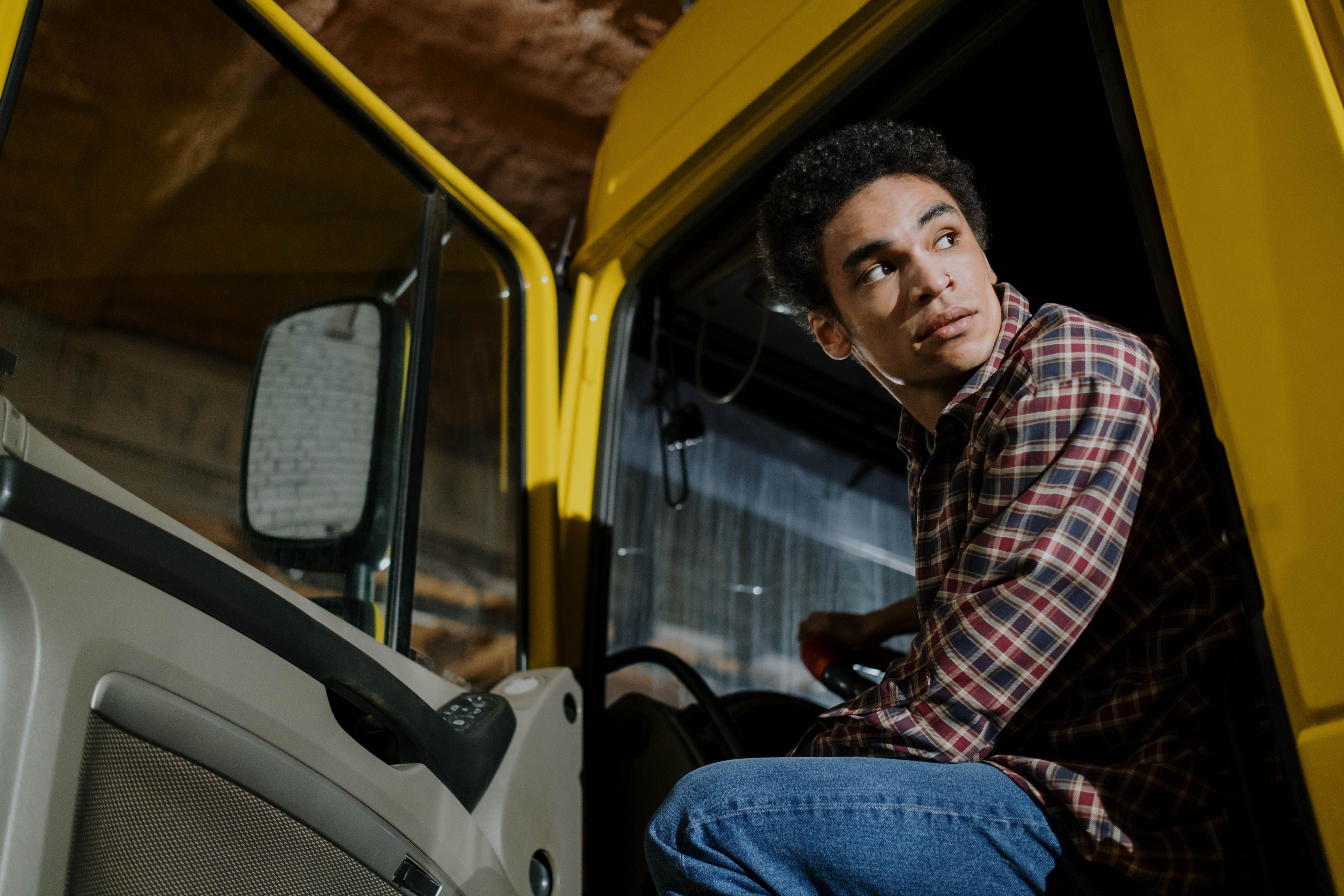 A truck driver in a plaid shirt seated inside a modern semi-truck cab